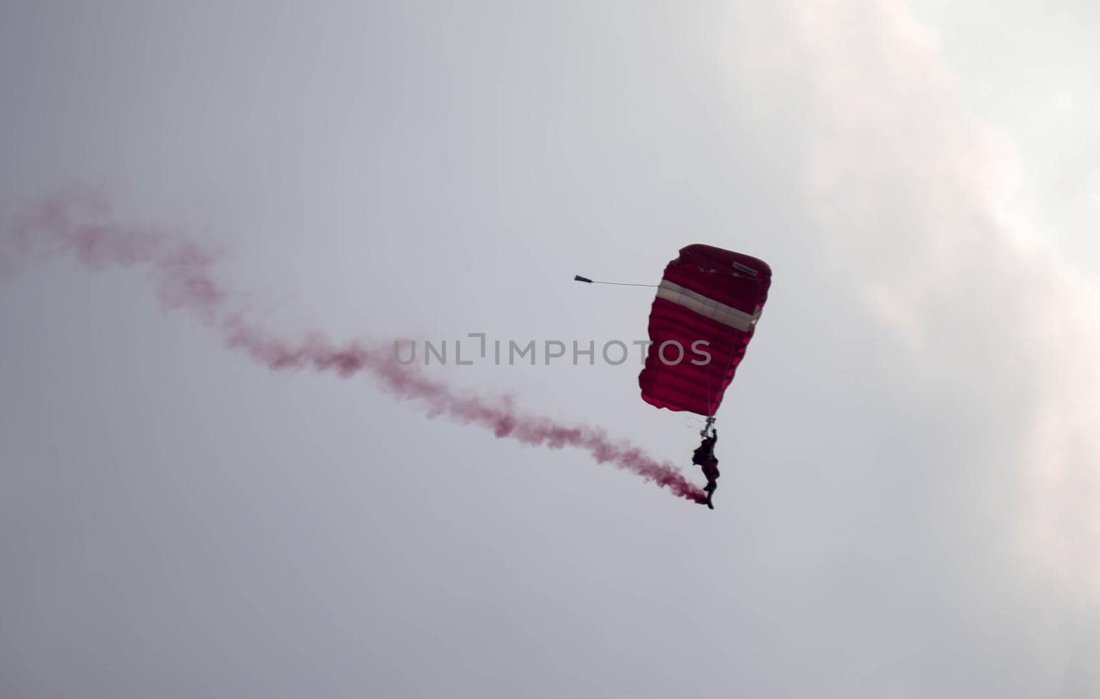 silhouette parachute stunt unfocused and blurry while gliding in the air with red smoke trail during an air exhibition in Singapore