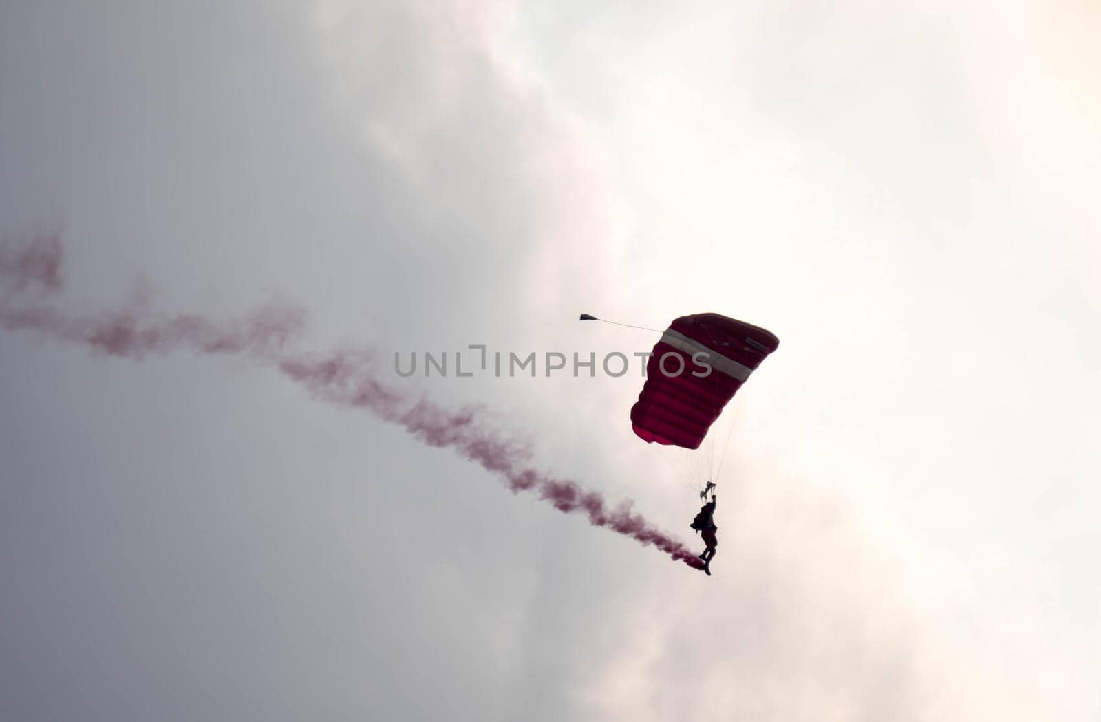 silhouette parachute stunt unfocused and blurry while gliding in the air with red smoke trail during an air exhibition in Singapore