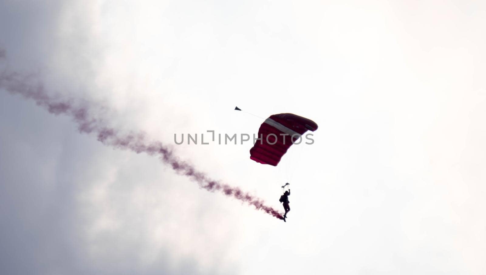 silhouette parachute stunt unfocused and blurry while gliding in the air with red smoke trail during an air exhibition in Singapore