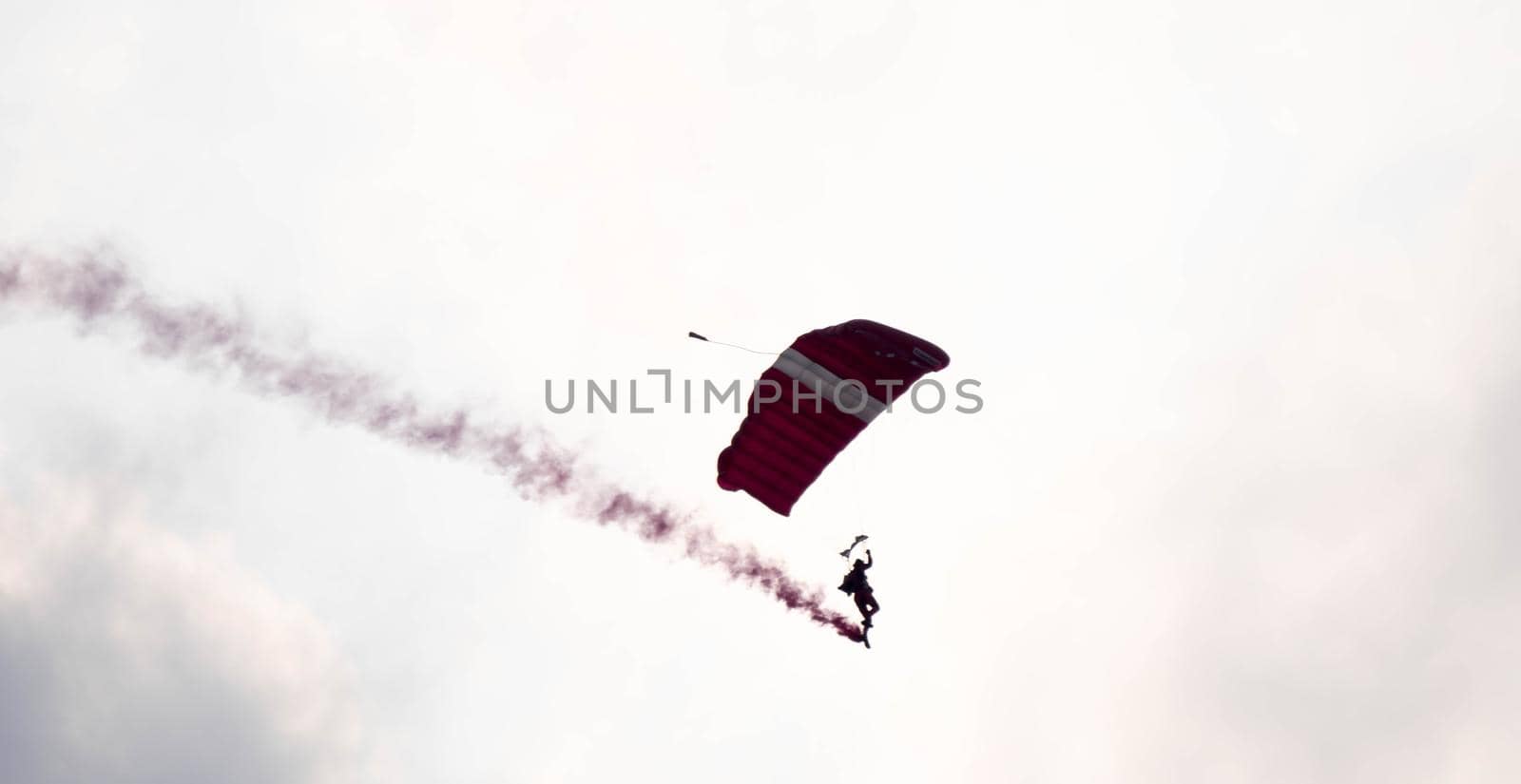 silhouette parachute stunt unfocused and blurry while gliding in the air with red smoke trail during an air exhibition in Singapore