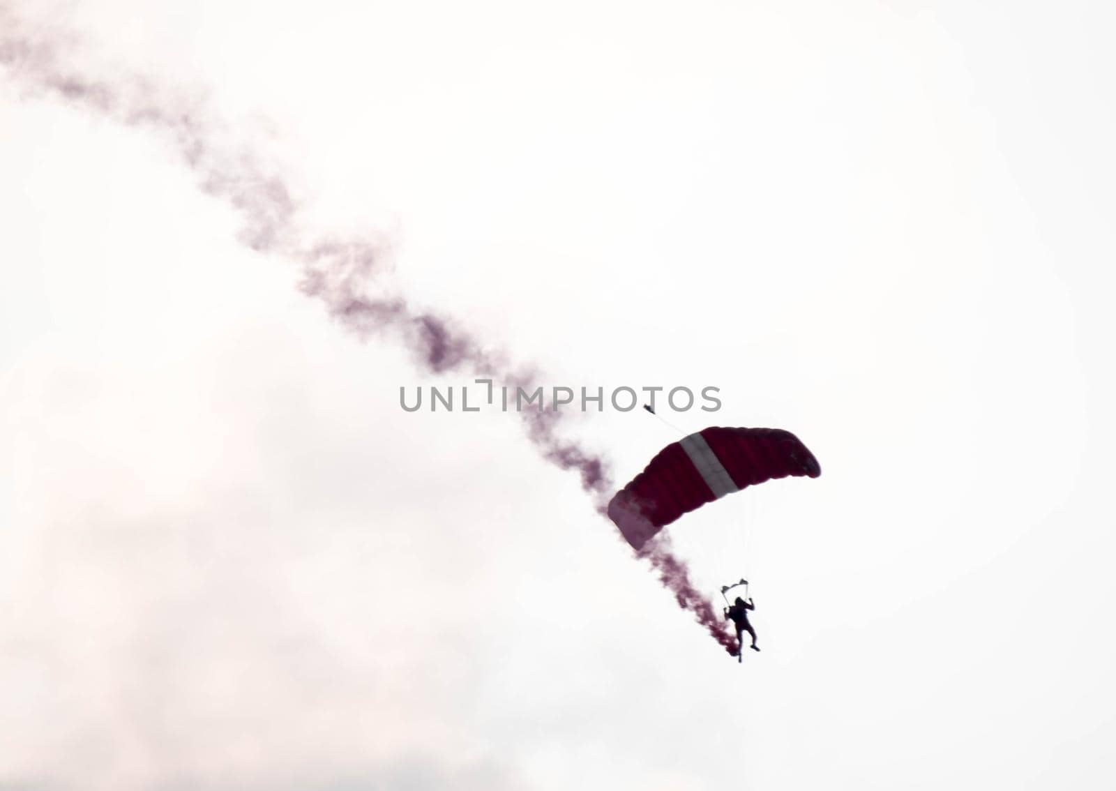 silhouette parachute stunt unfocused and blurry while gliding in the air with red smoke trail during an air exhibition in Singapore