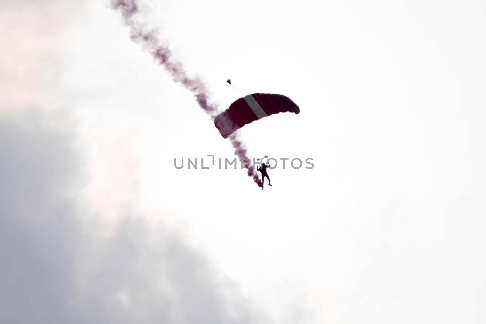 silhouette parachute stunt unfocused and blurry while gliding in the air with red smoke trail during an air exhibition in Singapore