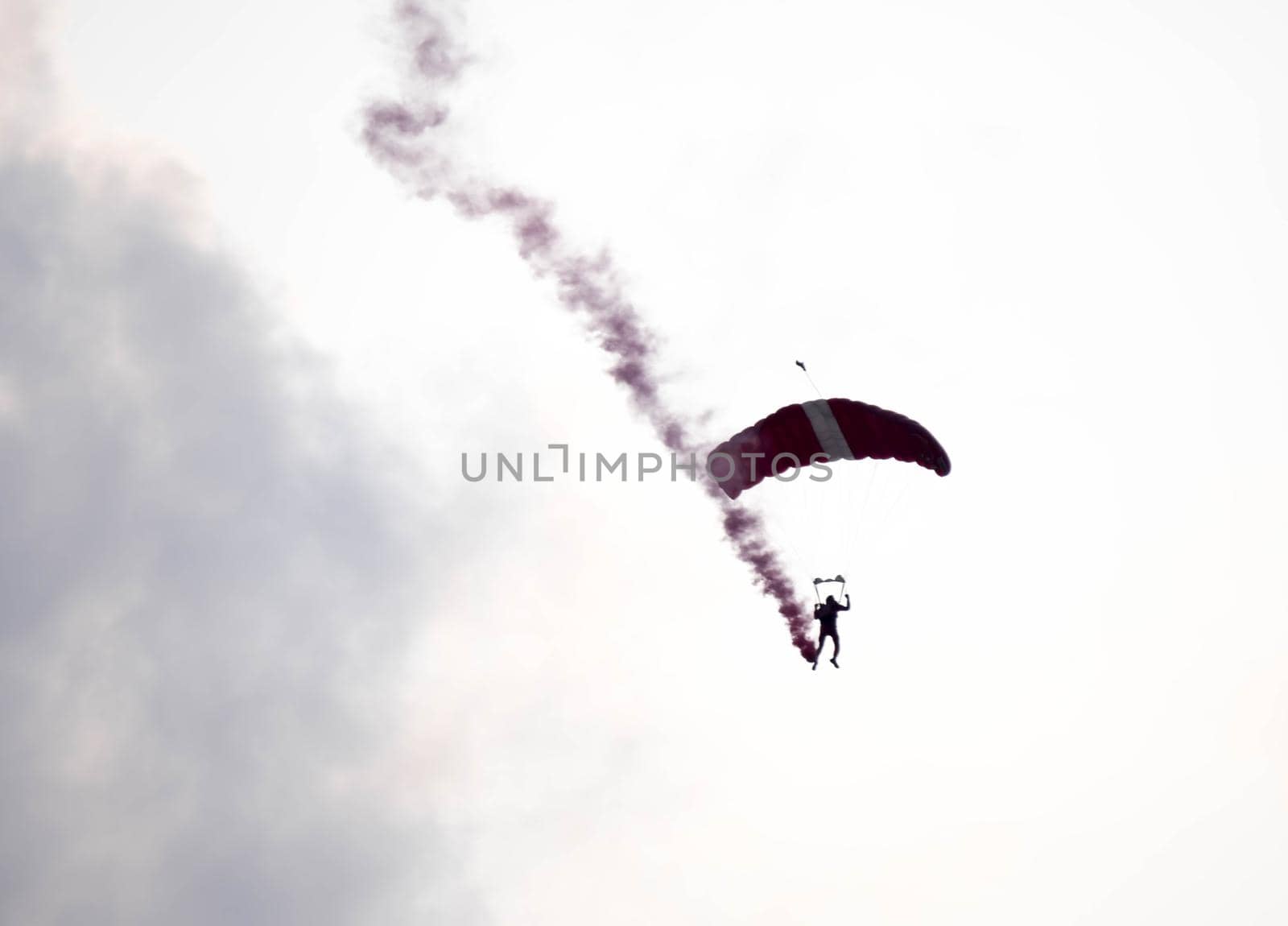 silhouette parachute stunt unfocused and blurry while gliding in the air with red smoke trail during an air exhibition in Singapore