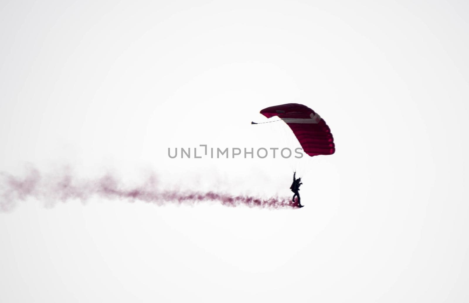 silhouette parachute stunt unfocused and blurry while gliding in the air with red smoke trail during an air exhibition in Singapore