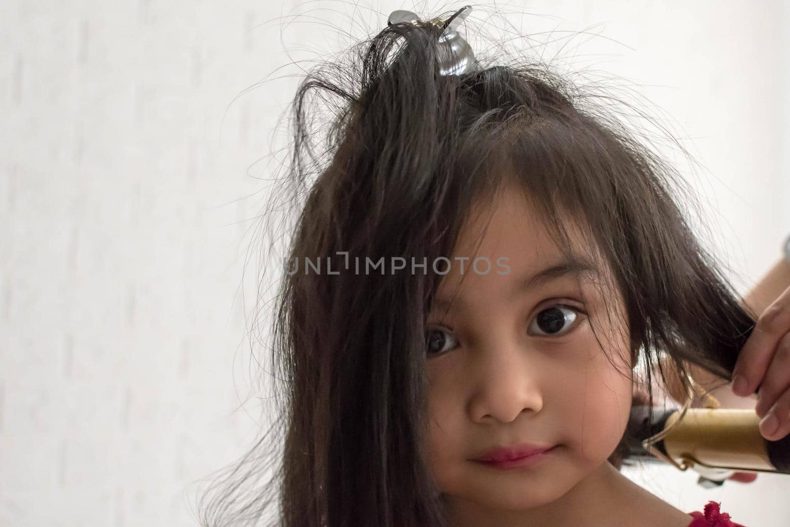 Stylist curling hair for little girl in a parlor by billroque