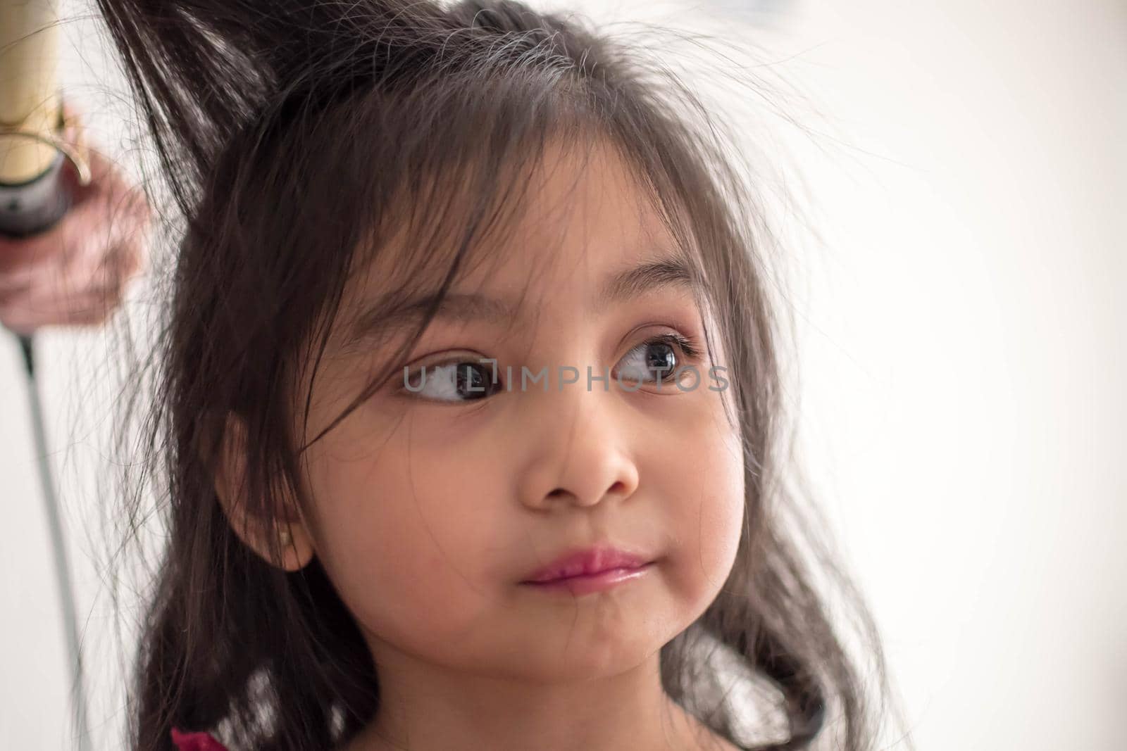 Stylist curling hair for little girl in a parlor. Pretty little girl with curly hair and make up