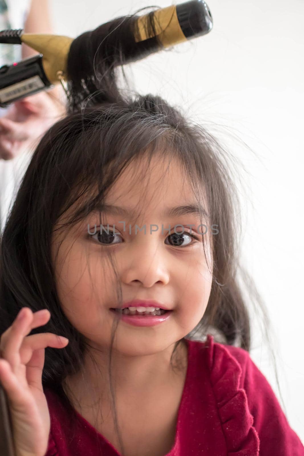 Stylist curling hair for little girl in a parlor. Pretty little girl with curly hair and make up