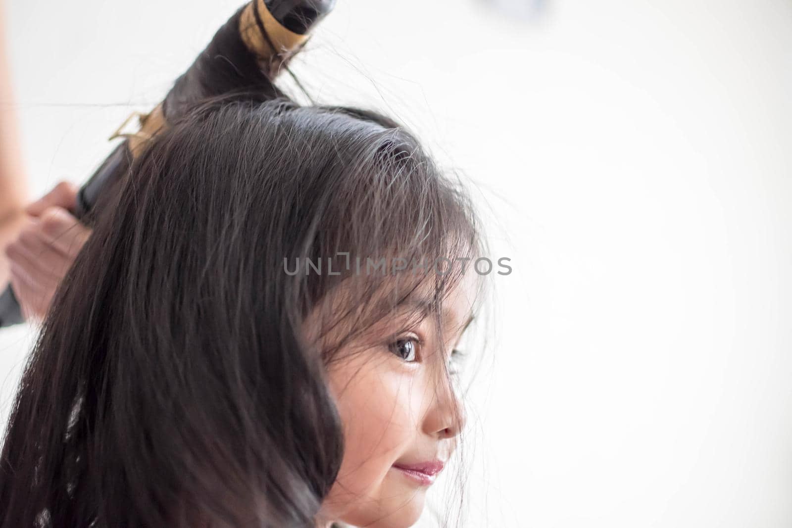 Stylist curling hair for little girl in a parlor. Pretty little girl with curly hair and make up