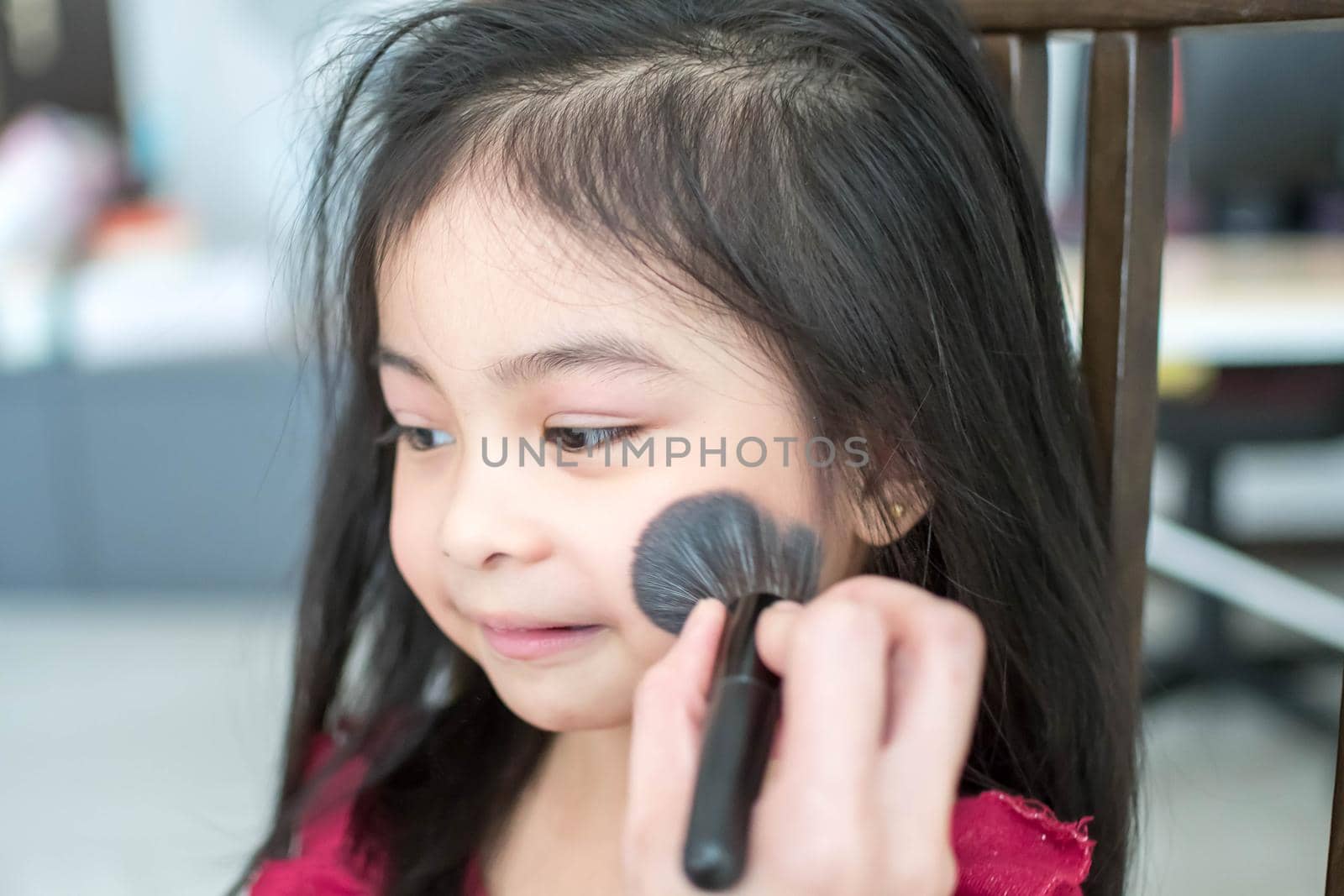 Pretty cute little girl while having a makeup, lipstick and blush on