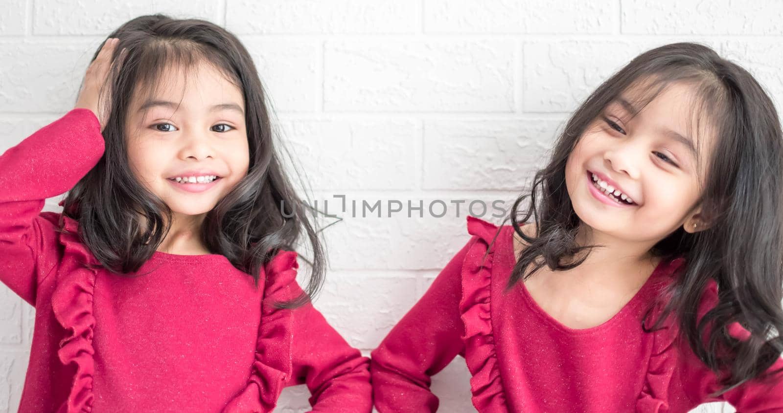 An Identical twin girls sisters are posing for the camera. Happy twin sisters in dresses are looking at the camera and smiling. Frontal view, on white background