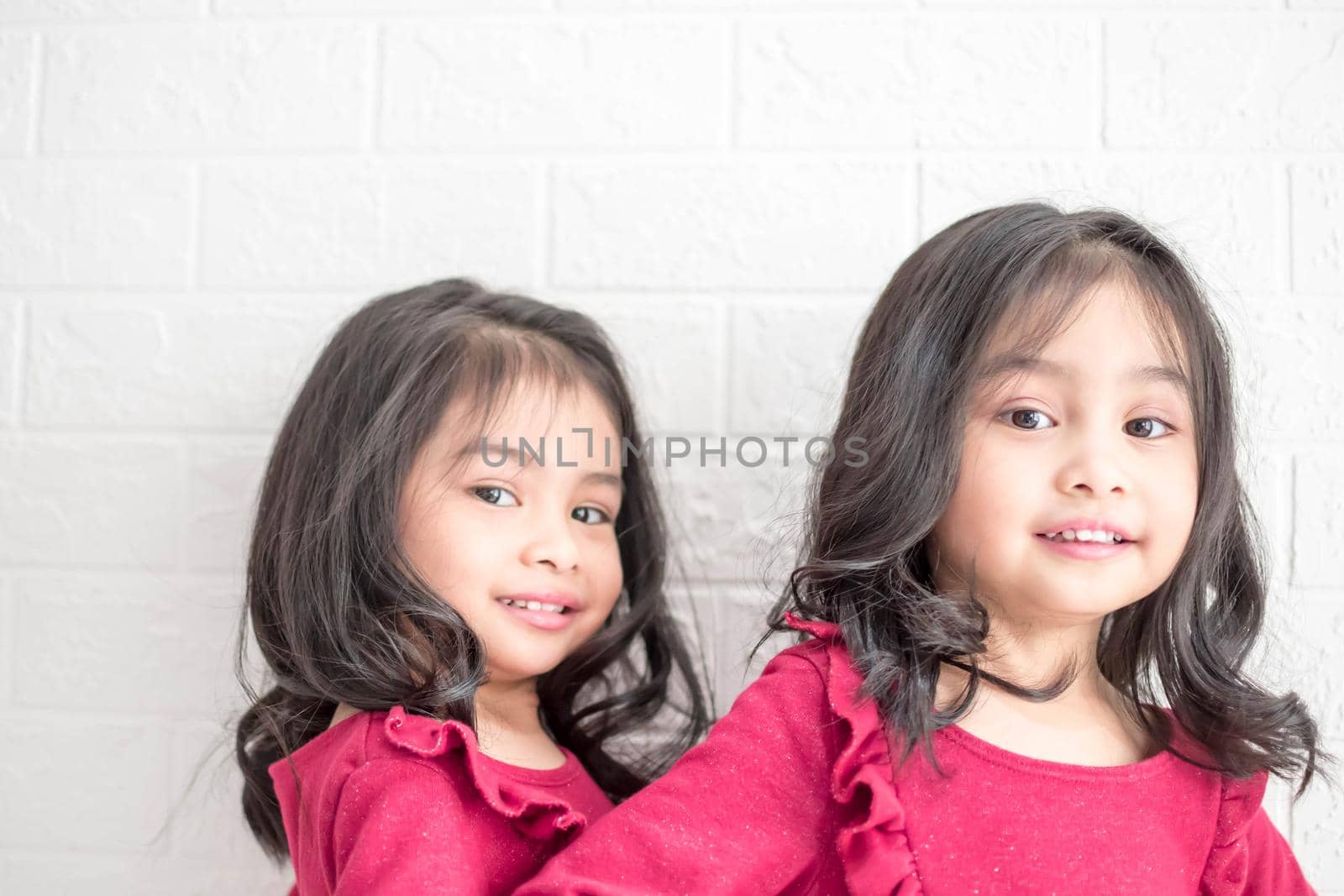 An Identical twin girls sisters are posing for the camera. Happy twin sisters in dresses are looking at the camera and smiling. Frontal view, on white background