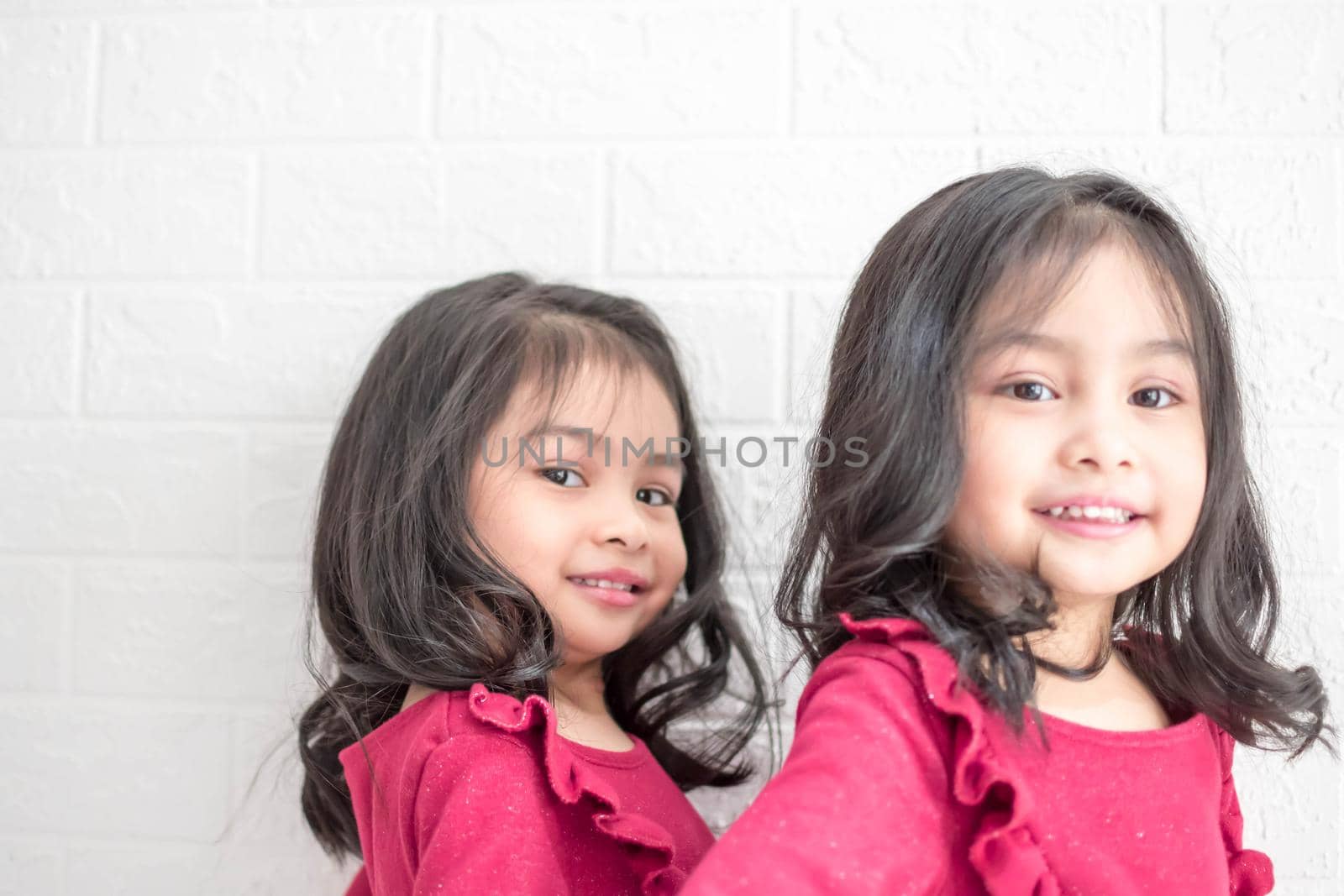 An Identical twin girls sisters are posing for the camera. Happy twin sisters in dresses are looking at the camera and smiling. Frontal view, on white background