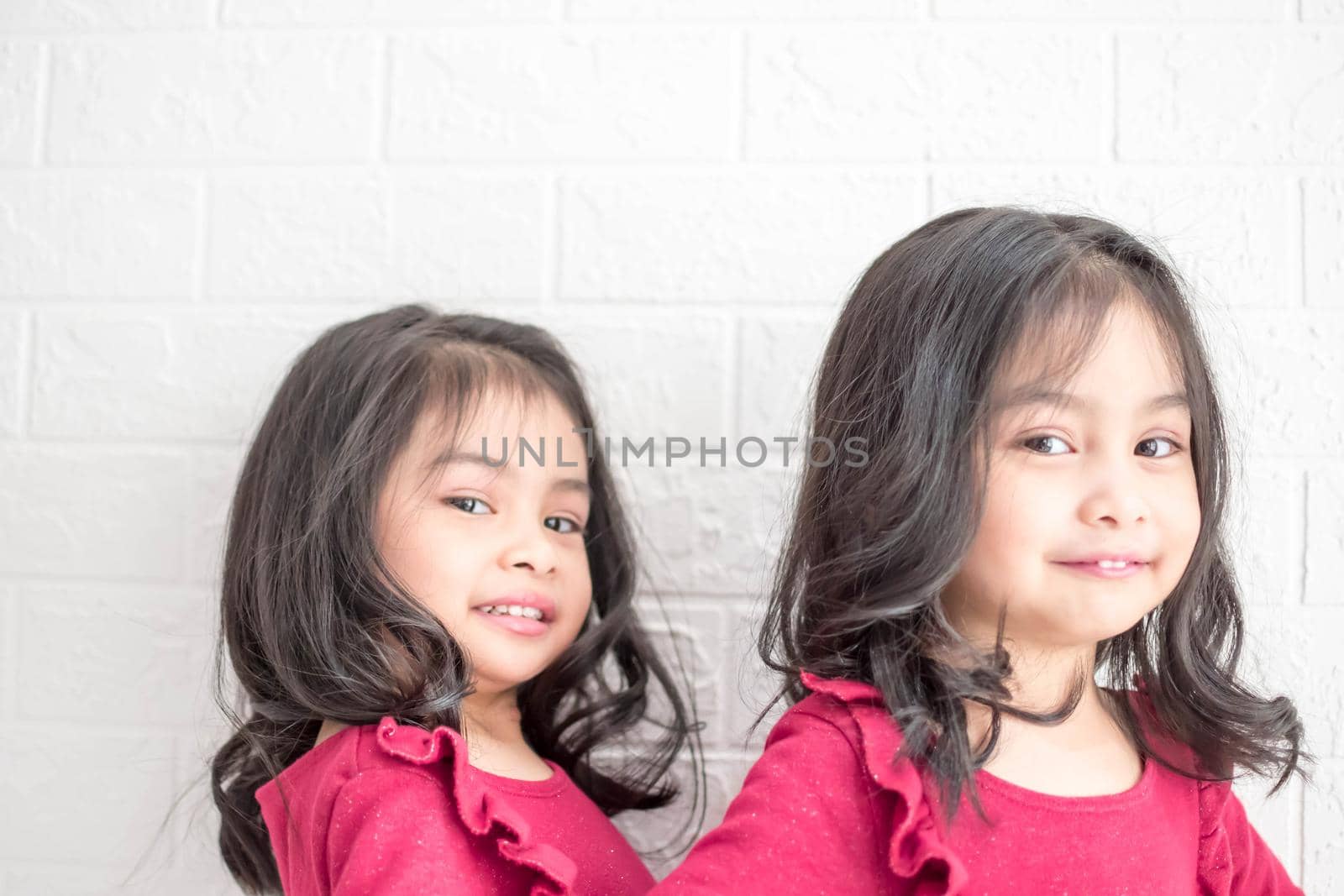 An Identical twin girls sisters are posing for the camera. Happy twin sisters in dresses are looking at the camera and smiling. Frontal view, on white background