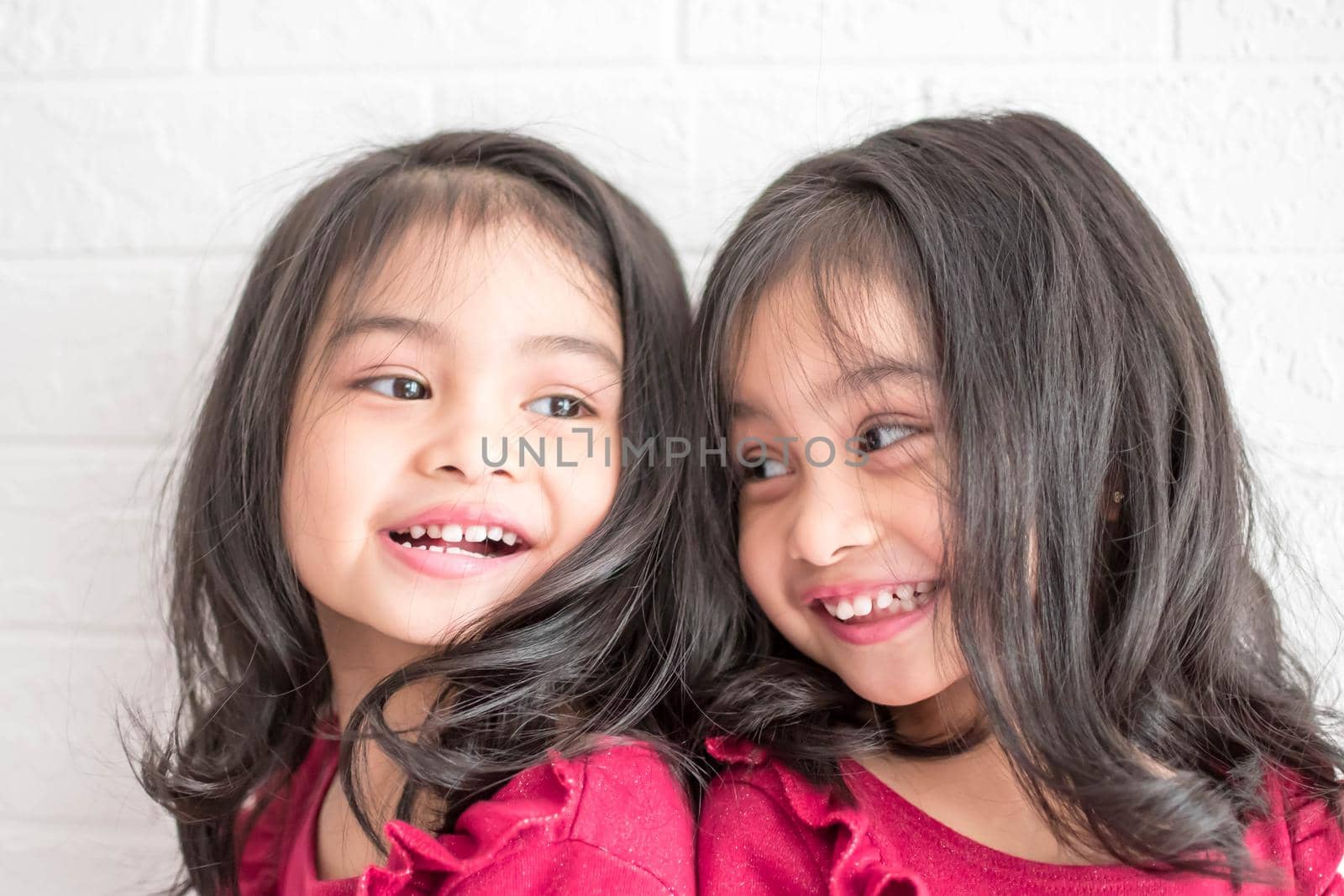 Identical twin girls sisters are posing for the camera. Happy twin sisters in dresses are looking at the camera and smiling. Frontal view, on white background by billroque