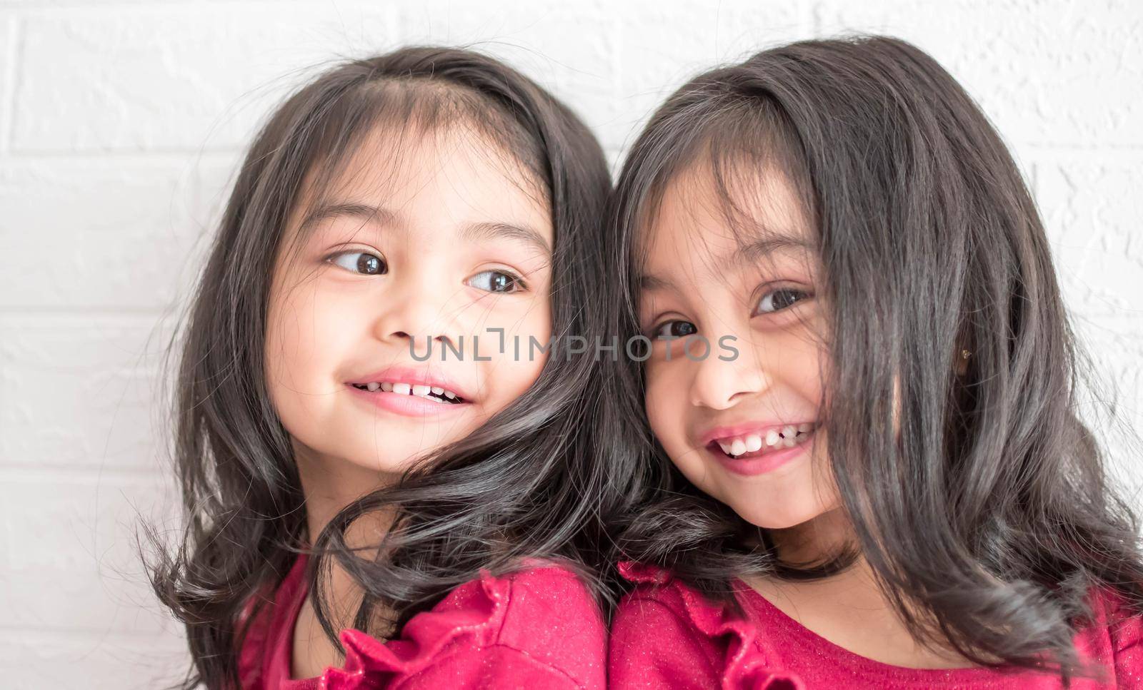 An Identical twin girls sisters are posing for the camera. Happy twin sisters in dresses are looking at the camera and smiling. Frontal view, on white background