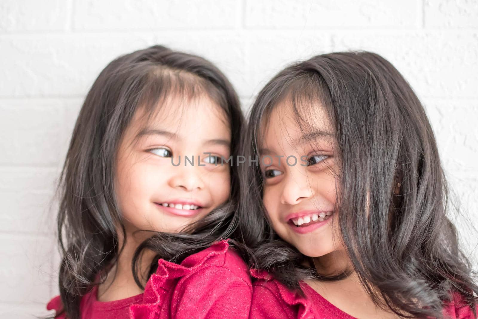 Identical twin girls sisters are posing for the camera. Happy twin sisters in dresses are looking at the camera and smiling. Frontal view, on white background by billroque