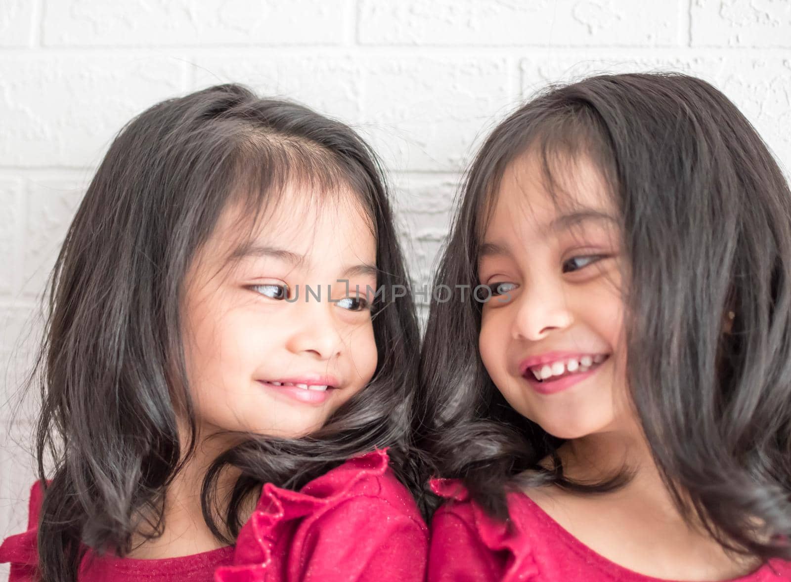 Identical twin girls sisters are posing for the camera. Happy twin sisters in dresses are looking at the camera and smiling. Frontal view, on white background by billroque