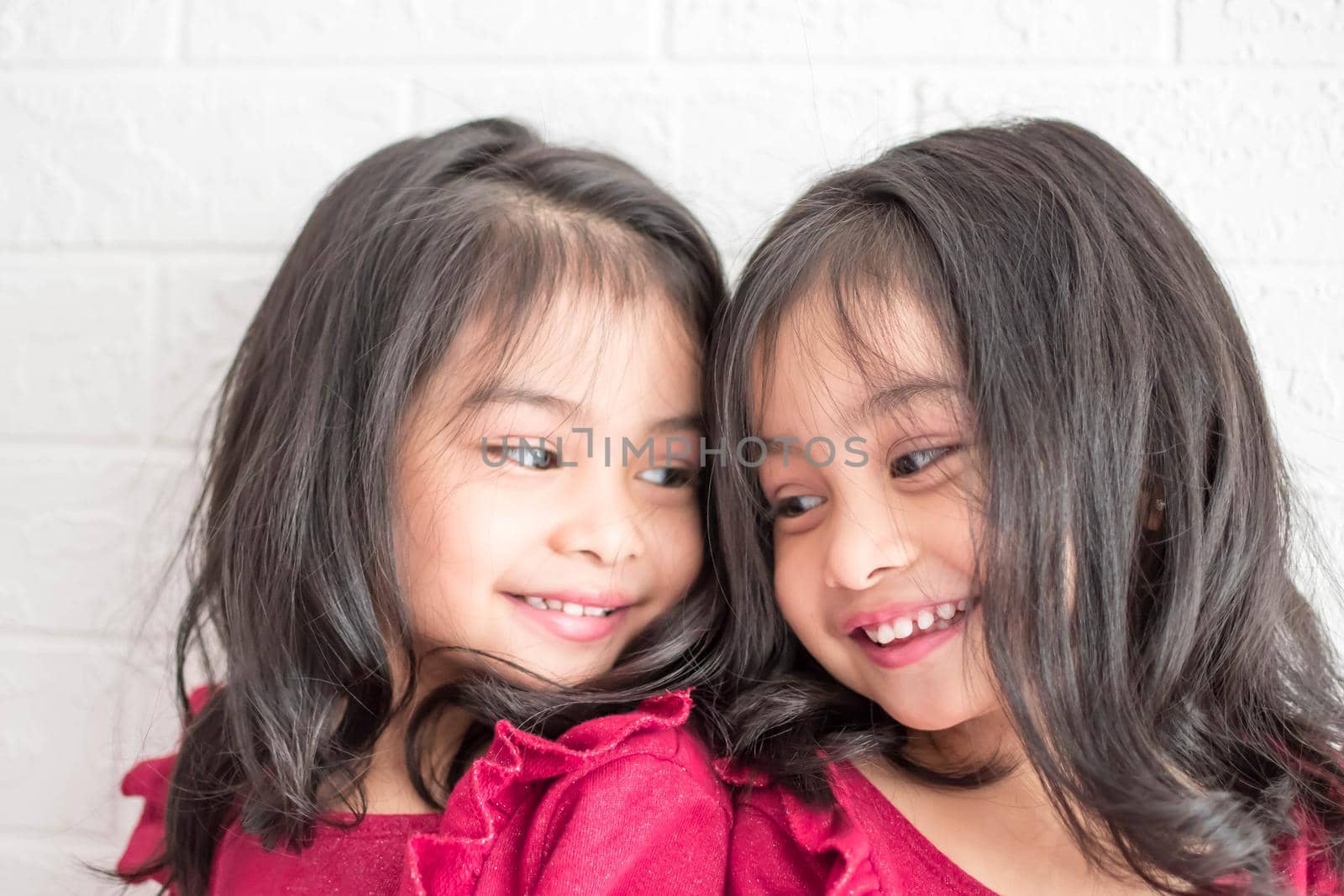 An Identical twin girls sisters are posing for the camera. Happy twin sisters in dresses are looking at the camera and smiling. Frontal view, on white background