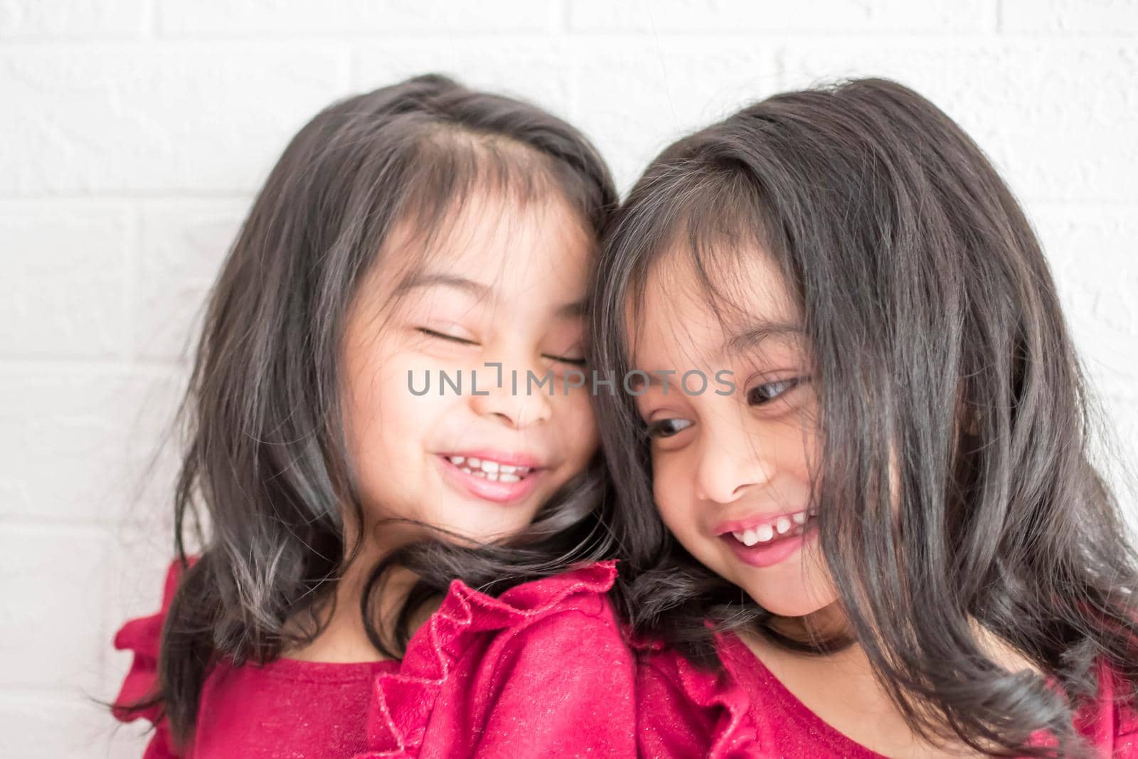 Identical twin girls sisters are posing for the camera. Happy twin sisters in dresses are looking at the camera and smiling. Frontal view, on white background by billroque