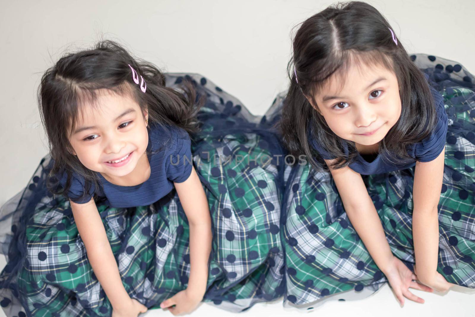 Identical twin girls sisters are posing for the camera. Happy twin sisters in dresses are looking at the camera and smiling. Frontal view, on white background by billroque