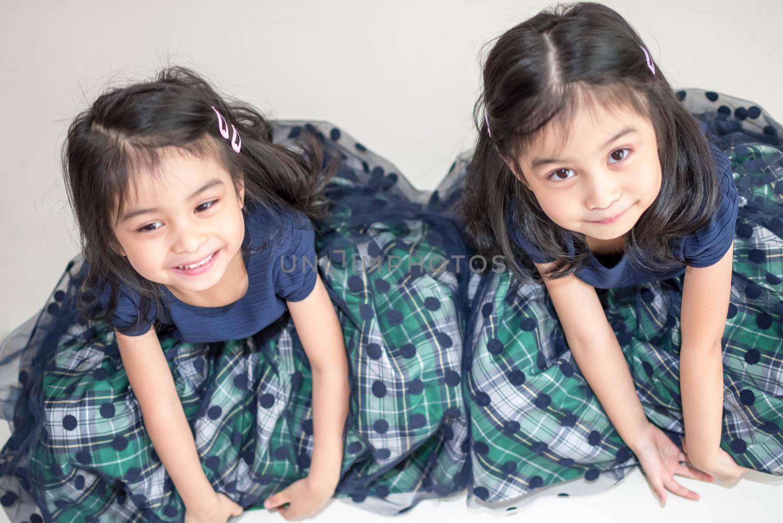 An Identical twin girls sisters are posing for the camera. Happy twin sisters in dresses are looking at the camera and smiling. Frontal view, on white background