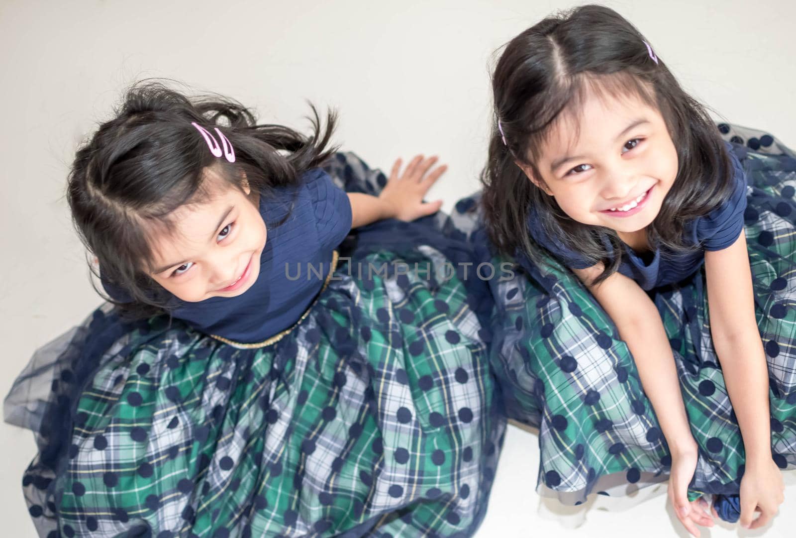 An Identical twin girls sisters are posing for the camera. Happy twin sisters in dresses are looking at the camera and smiling. Frontal view, on white background