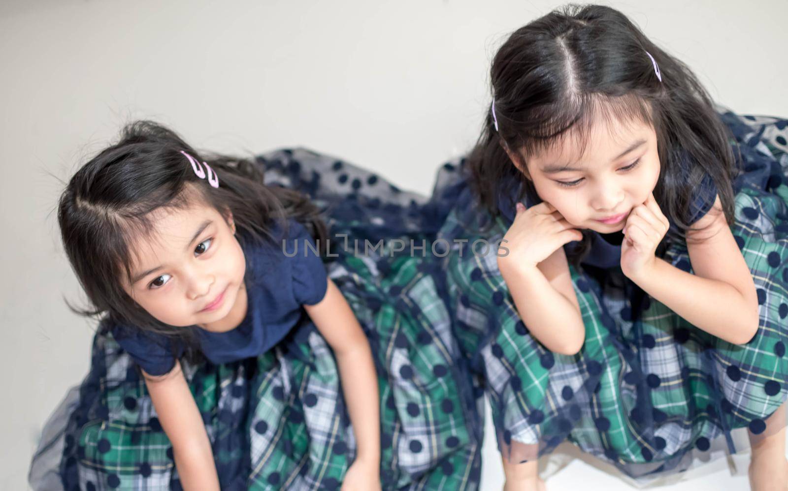 An Identical twin girls sisters are posing for the camera. Happy twin sisters in dresses are looking at the camera and smiling. Frontal view, on white background