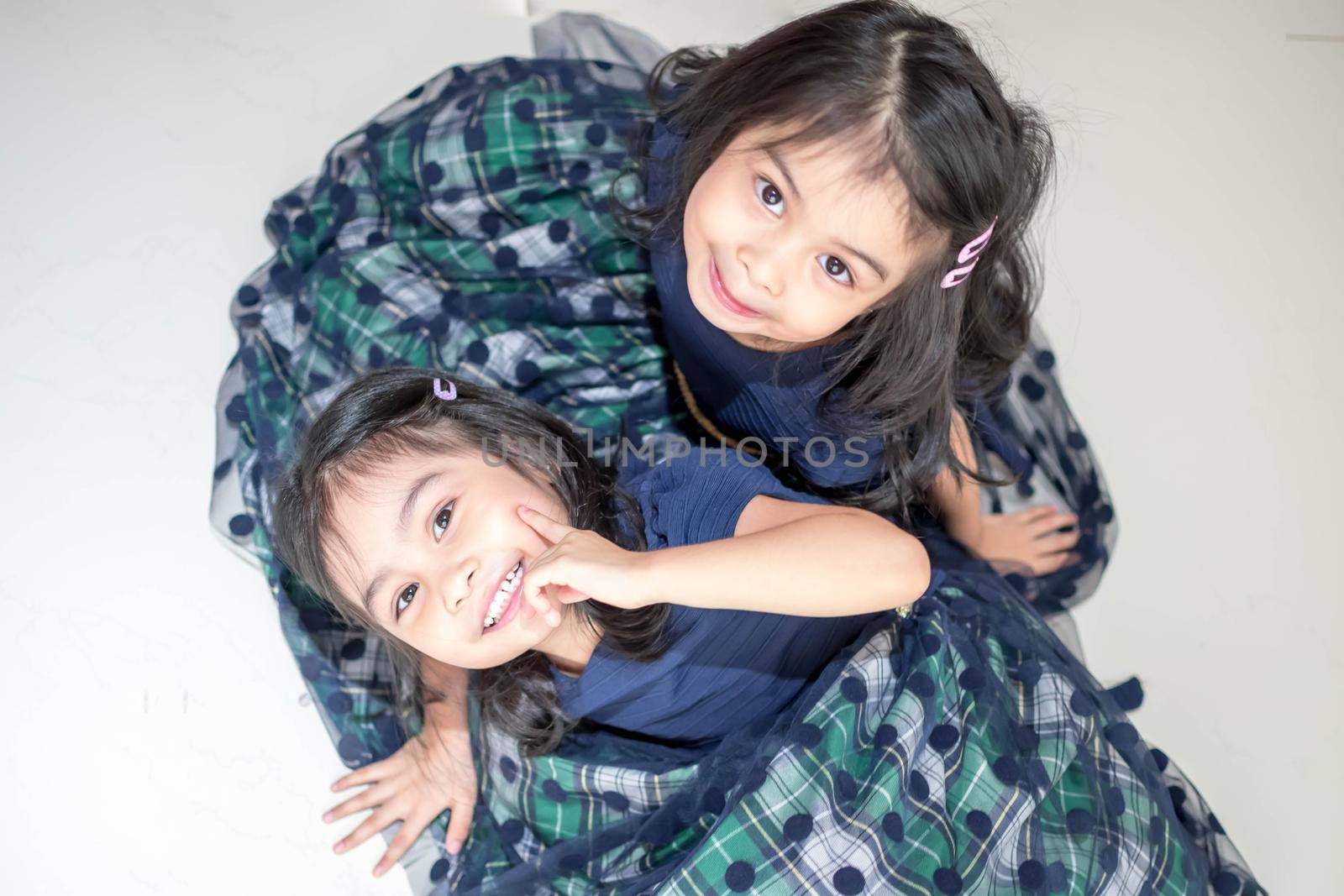 An Identical twin girls sisters are posing for the camera. Happy twin sisters in dresses are looking at the camera and smiling. Frontal view, on white background