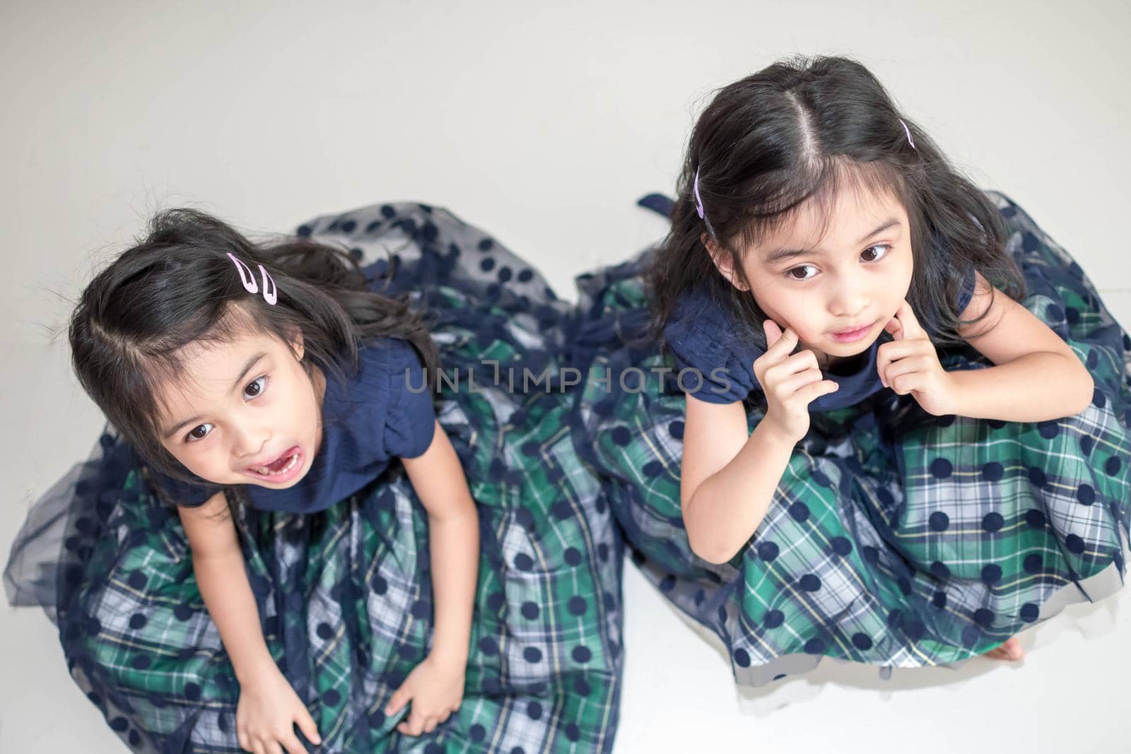 Identical twin girls sisters are posing for the camera. Happy twin sisters in dresses are looking at the camera and smiling. Frontal view, on white background by billroque