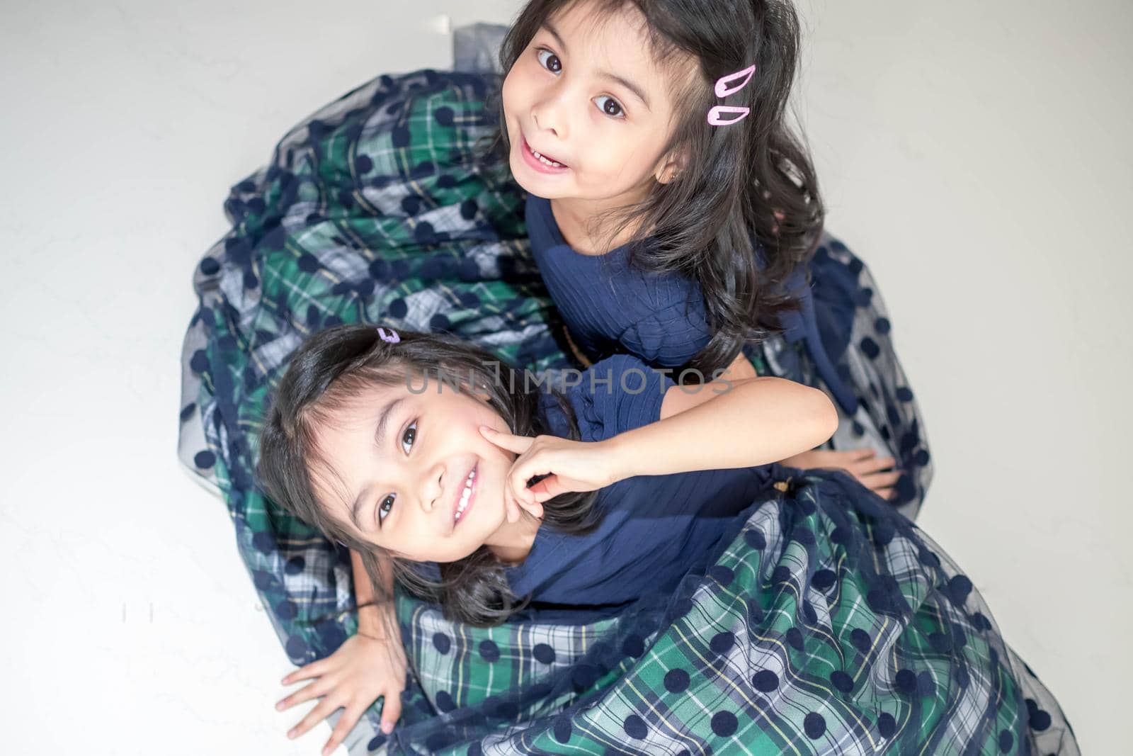 Identical twin girls sisters are posing for the camera. Happy twin sisters in dresses are looking at the camera and smiling. Frontal view, on white background by billroque