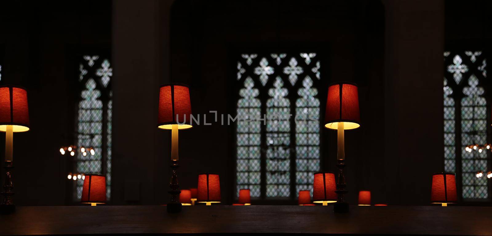 Calm empty dark church with mystic lights. Old Christian Church cathedral interior with red lamps and light through gothic arc windows in soft focus