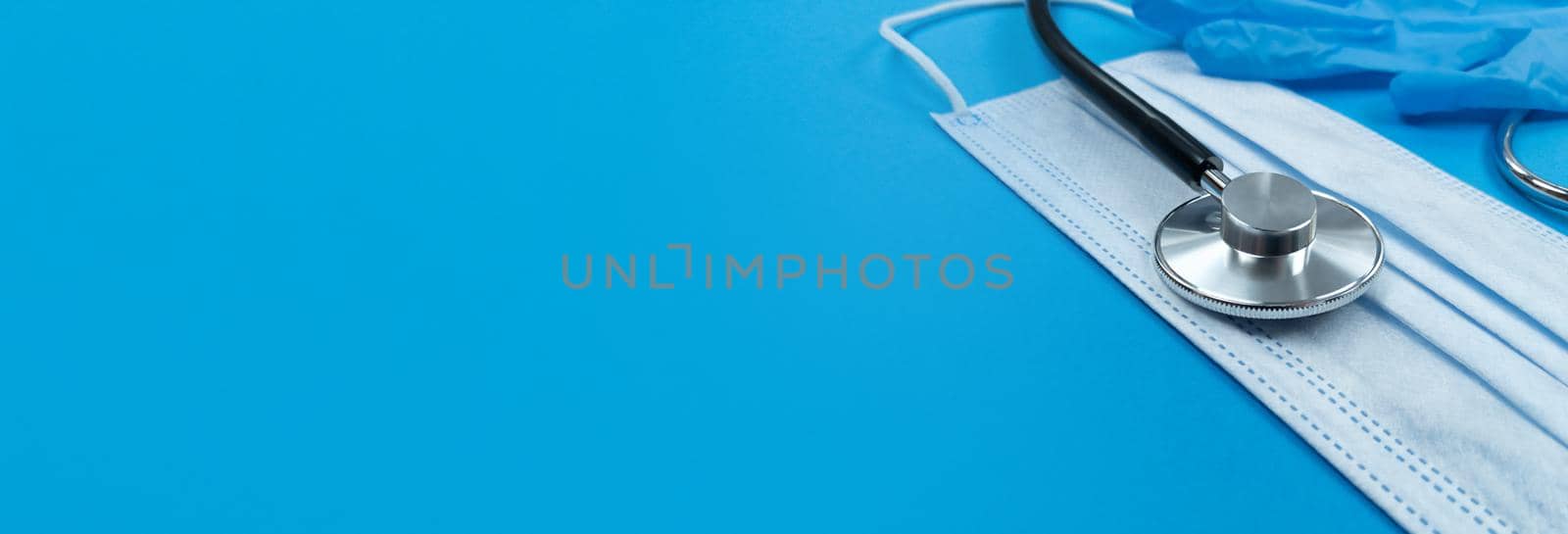 Stethoscope, face mask and medical gloves on a blue background. Medical banner with copy space.