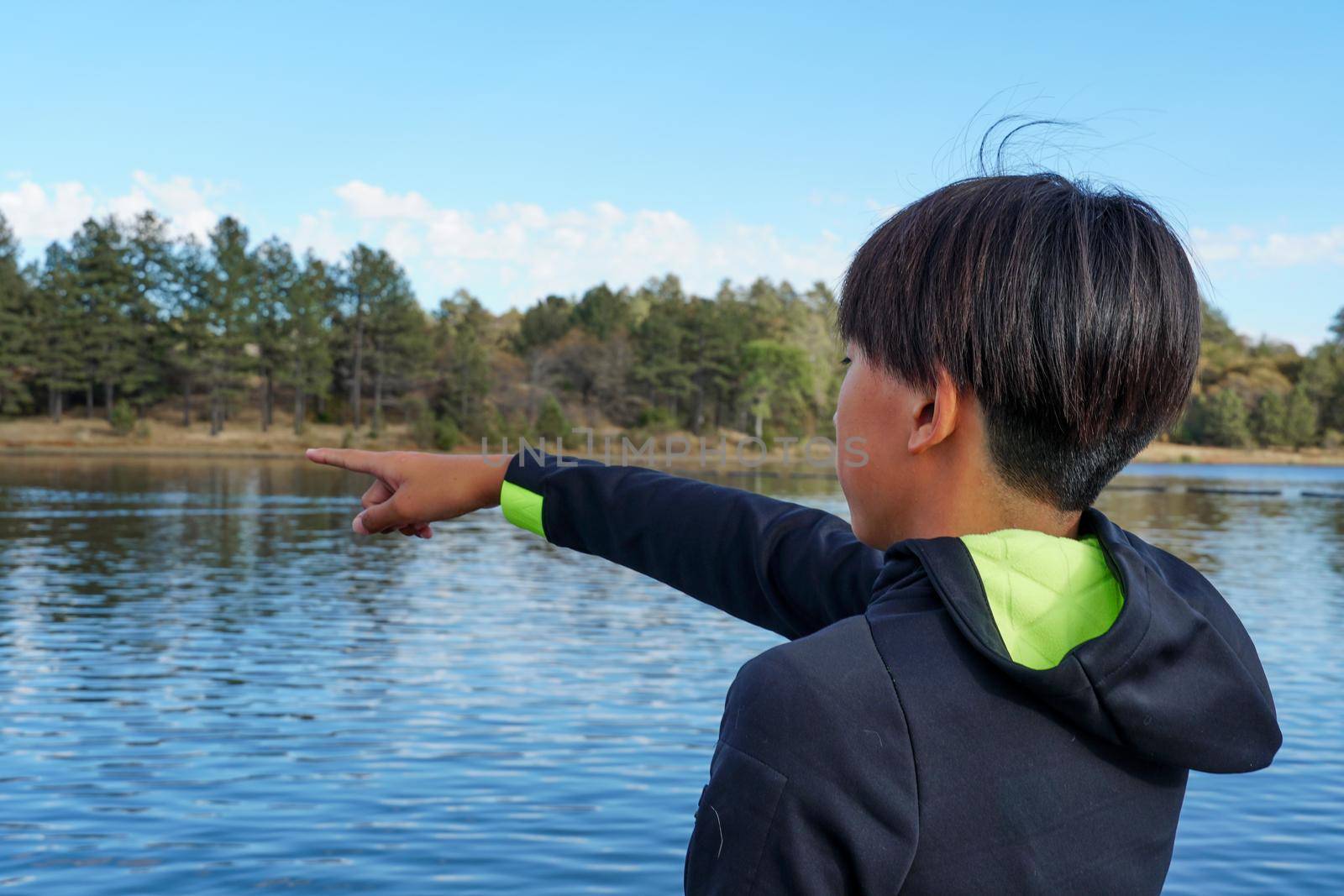 Young sporty Asian teenager pointing at something and looking at the view by the Lake. Teenager concept