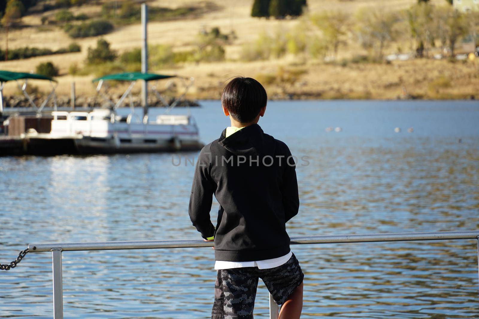 Young sporty Asian boy looking at the view on a wood pier at the Lake. by Bonandbon