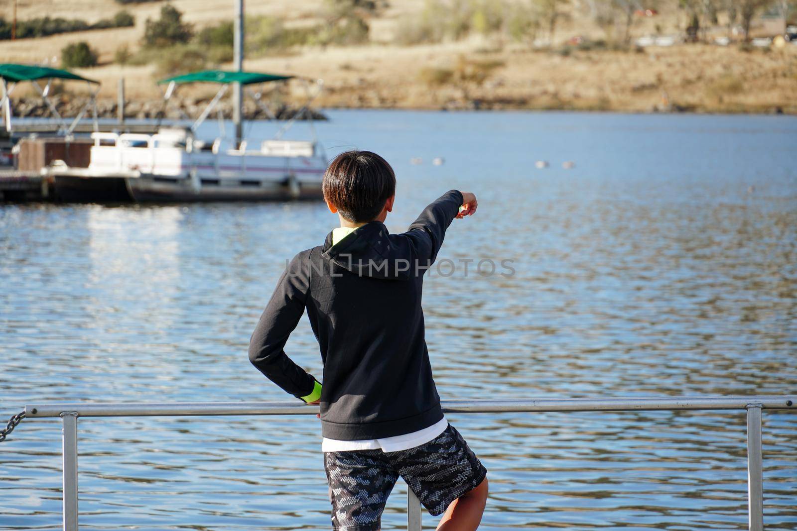 Young sporty Asian boy looking at the view on a wood pier at the Lake. by Bonandbon