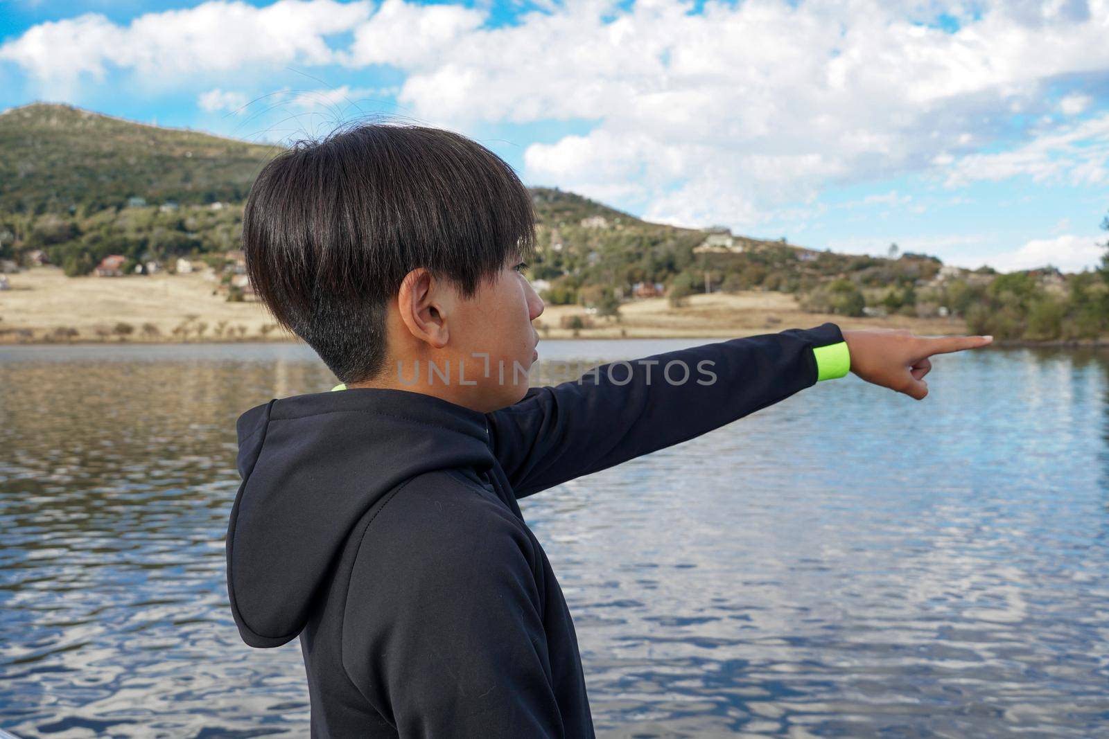 Young sporty Asian teenager pointing at something and looking at the view by the Lake. Teenager concept