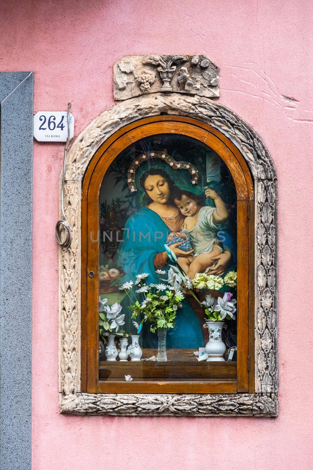 Decorated votive shrine of Virgin Mary and Jesus on a pink house wall, Zafferana Etnea, Italy