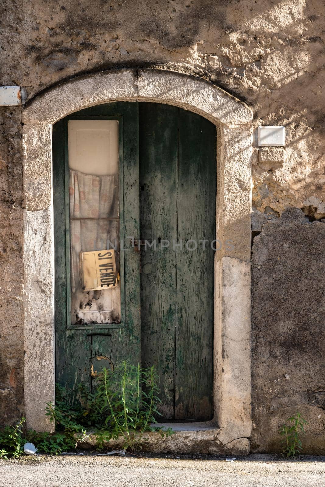Old wooden door of an abandoned house with a 'for sale' sign, Italy by mauricallari