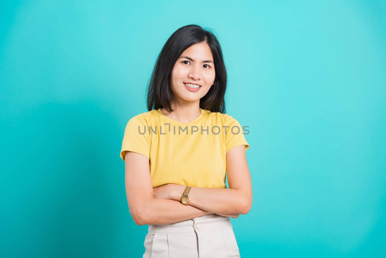 Portrait Asian beautiful young woman standing smile seeing white teeth, She crossed her arms and looking at camera, shoot photo in studio on blue background. copy space to put text on left-hand side.