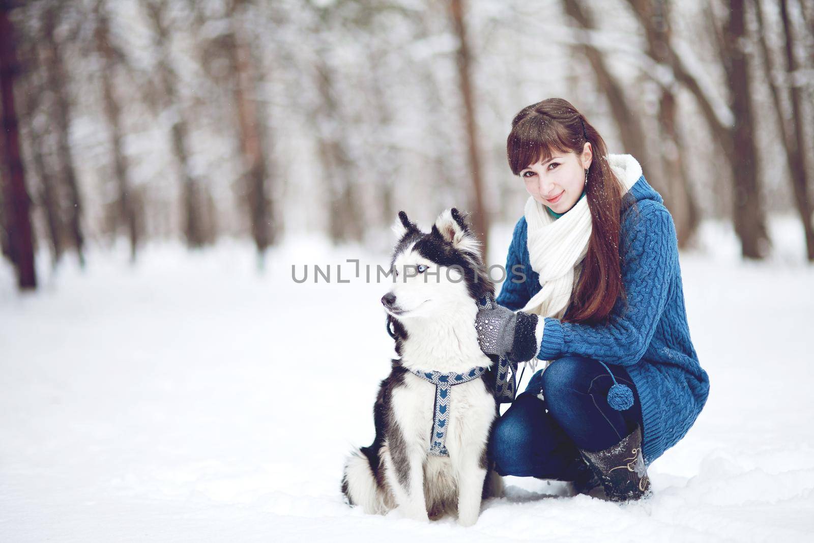 Girl sitting in the snow with a siberian husky dog in the winter forest by selinsmo