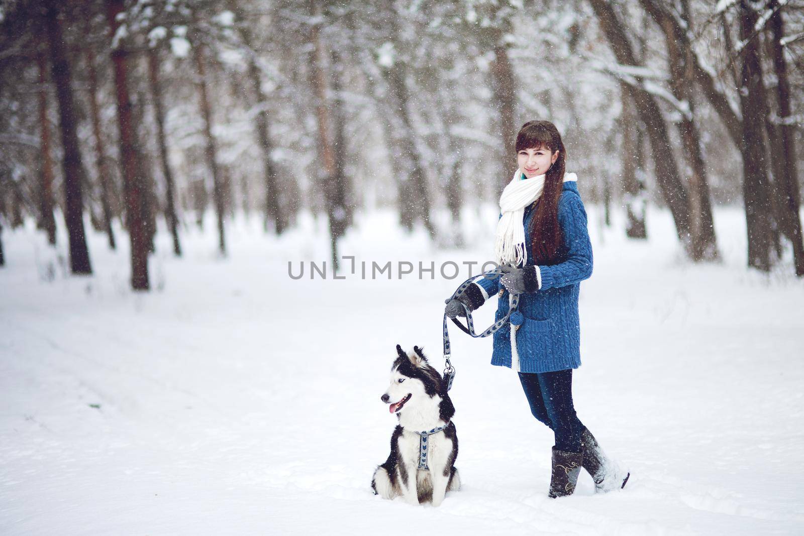 The girl walks with dog siberian husky in a winter snowy forest. 