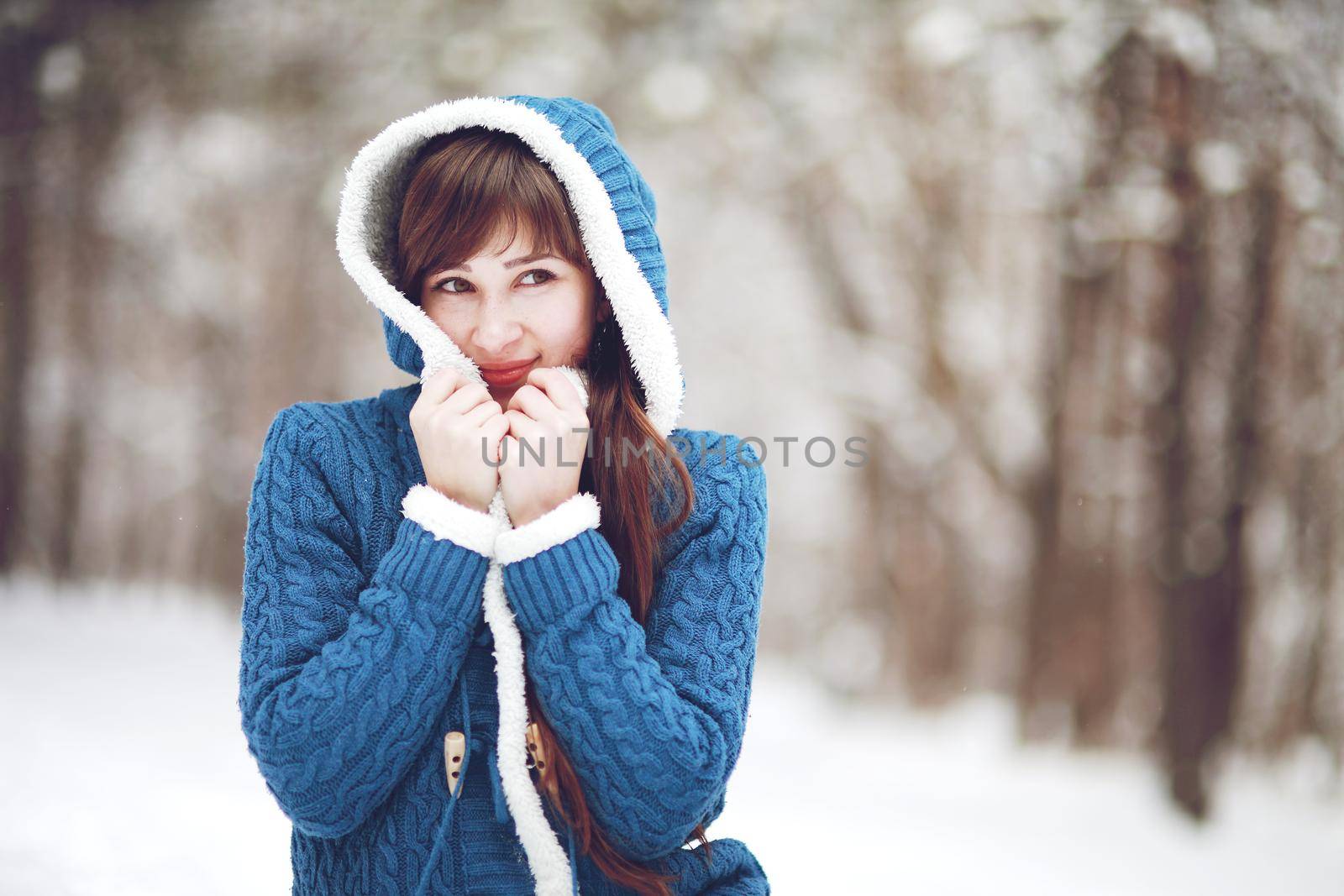 Winter portrait of a lovely girl in a blue sweater on the background of a snowy forest.
