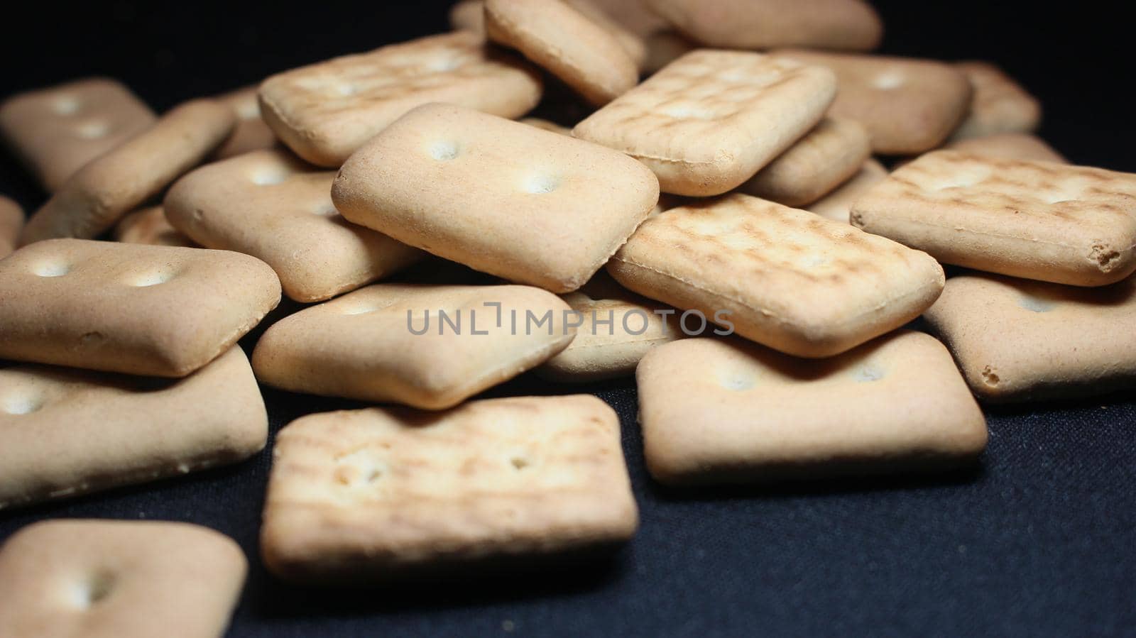 Close up top view of of biscuit cookies. Many rectangular biscuits with small pores on black floor