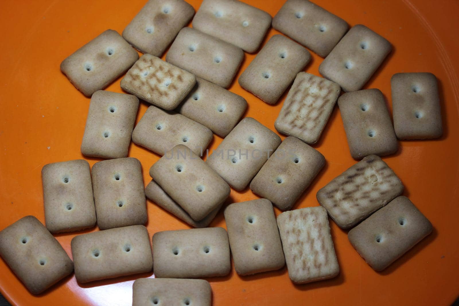 Close up top view of of biscuit cookies. Many rectangular biscuits with small pores in red plate
