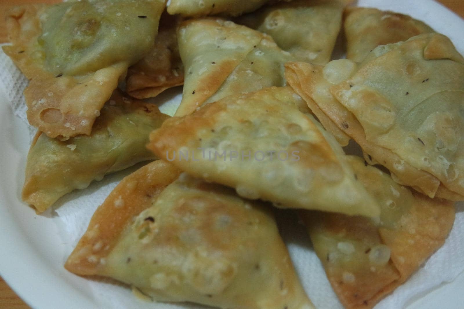 Closeup of delicious home made spicy and crunchy samosa pastries placed in a white ceramic plate on wooden floor