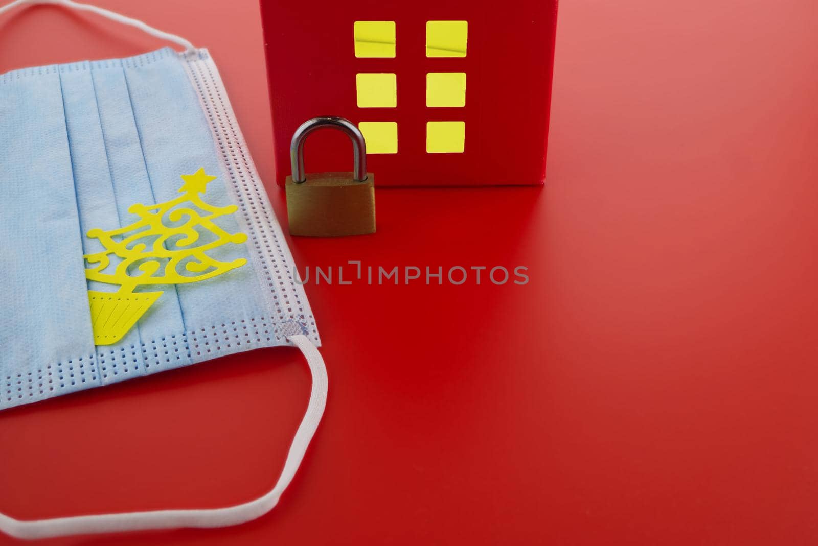 Epidemic, social isolation, coronavirus COVID-19 concept with brass padlock, medical face mask and red house with light shining through the windows and free copy space for text