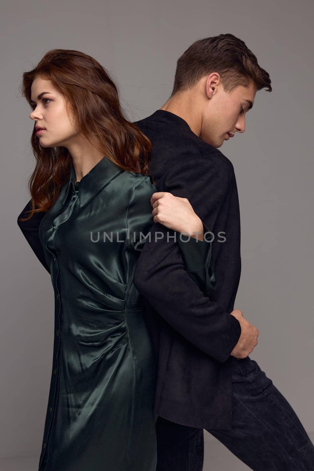 An elegant woman holds the hand of a man in a suit on a gray background with backs to each other by SHOTPRIME