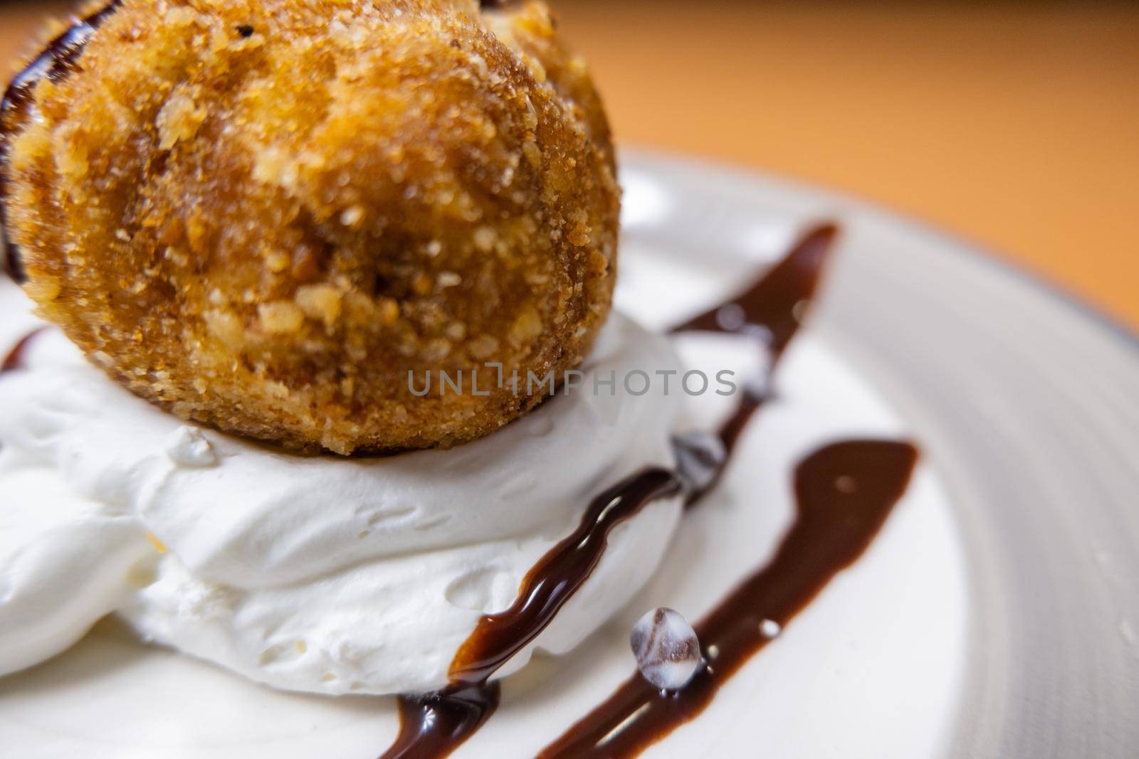 Close-up of fried ice cream with chocolate syrup, silver chocolate chips, and cream on white plate. Crispy Mexican fried ice cream scoop decorated with chocolate. Gourmet desserts