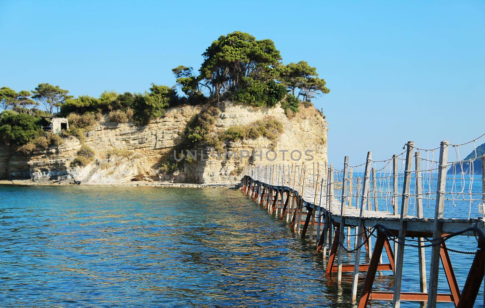 Wooden bridge leading to rocky island surrounded by blue sea. Greece, resort, Greek island Zakynthos