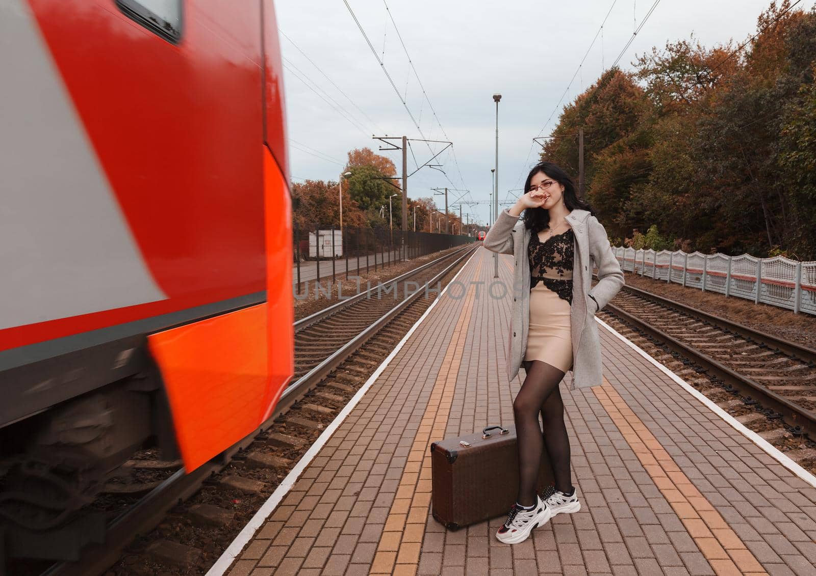 young girl in gray coat with suitcase standing at railway station by raddnatt